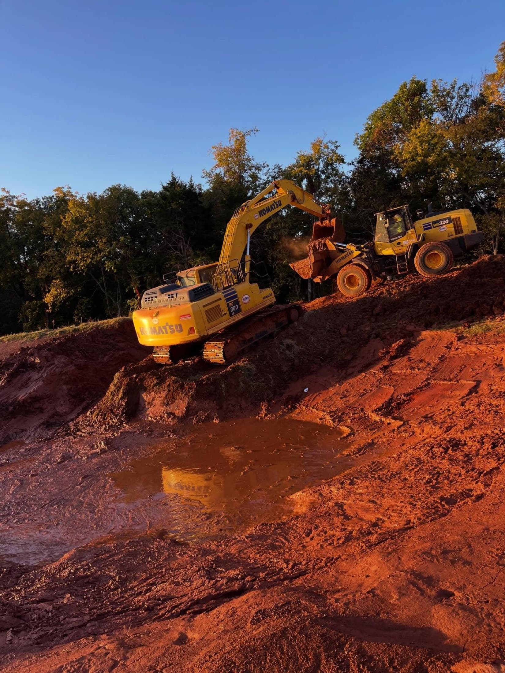 Excavator and loader moving material at sunset