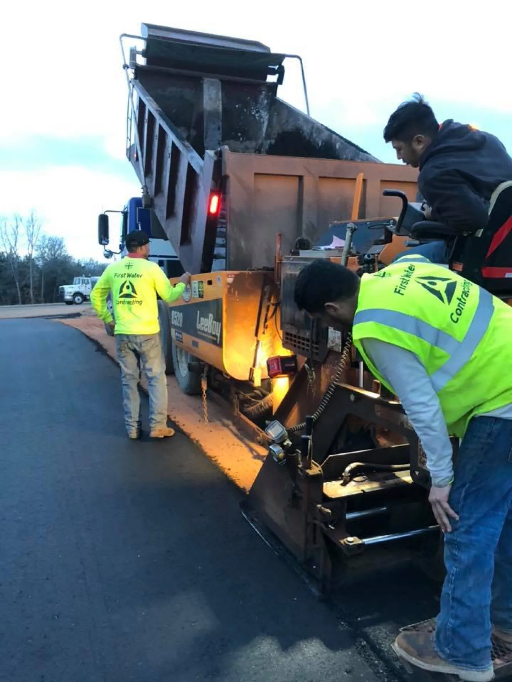 A First Water crew running a Leeboy asphalt paver at dusk